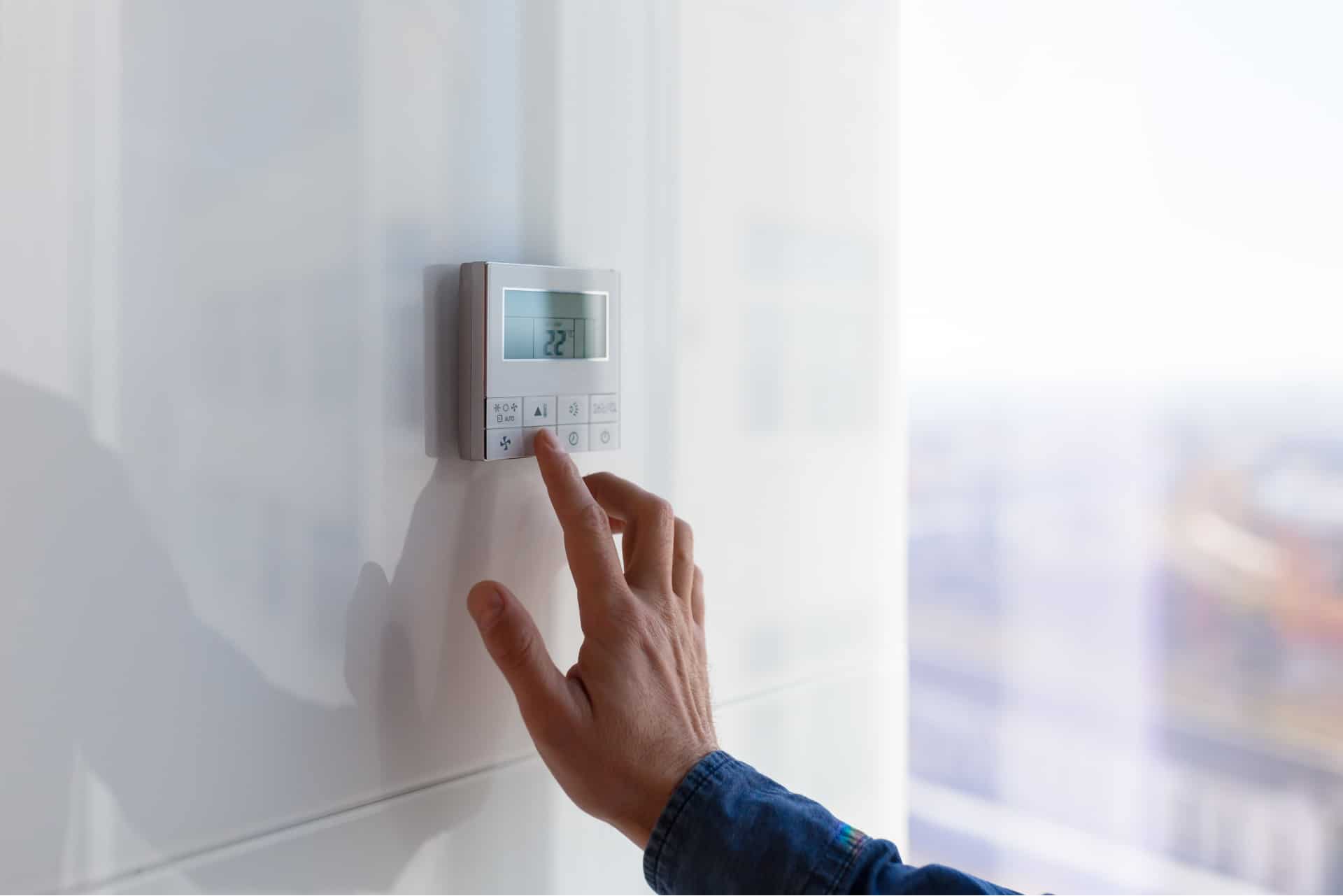 Person adjusting digital thermostat on wall