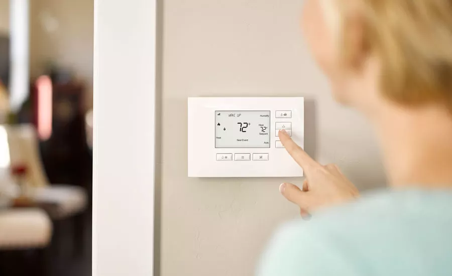 Person adjusting a digital thermostat on wall